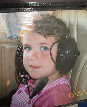 Hannah as a toddler wearing a pilot headset in a small plane