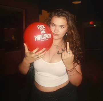 Hannah holding a red balloon that reads 'fuck the patriarchy'