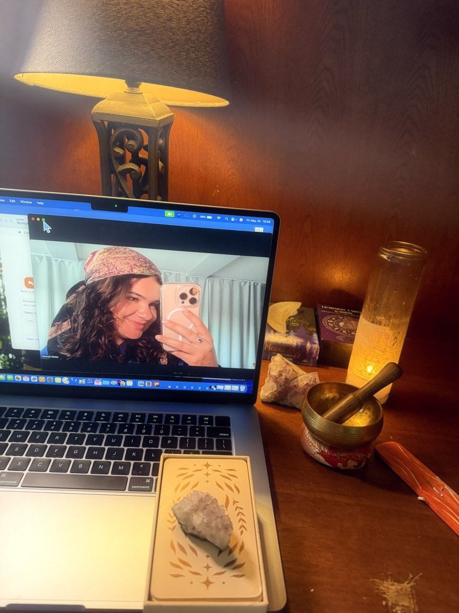 Hannah's reading desk: a live video session on her laptop, a lamp, oracle decks, crystals, a candle and a singing bowl