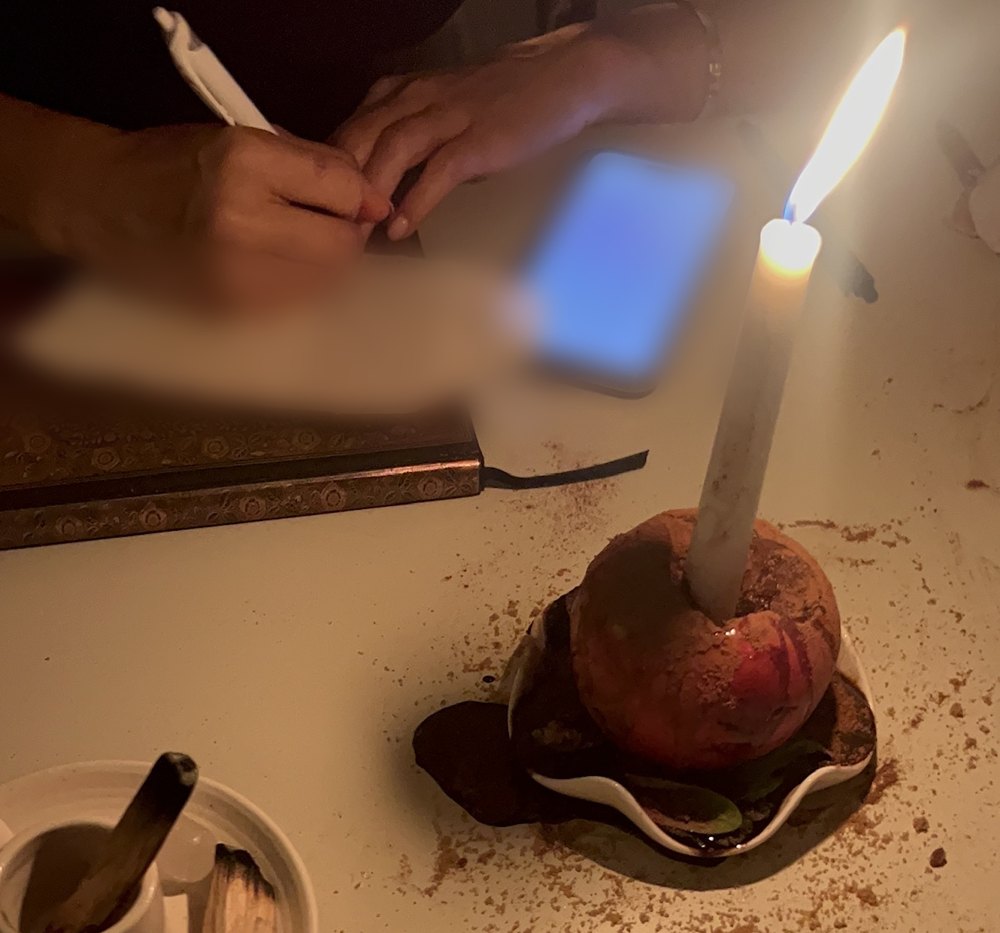 A white candle burning in a cinnamon-dusted apple beside palo santo and a journal