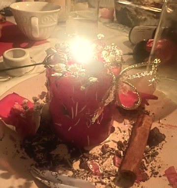 A hand-dressed red ritual candle with herbs and petals