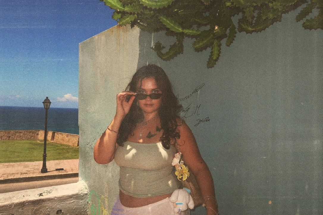 Hannah lowering her sunglasses by a seaside wall