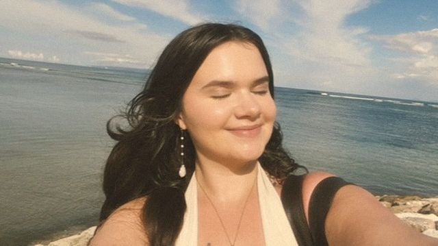 Hannah smiling with her eyes closed by the ocean